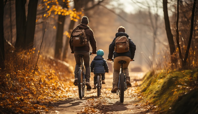 Two adults and a child cycling on a golden forest path