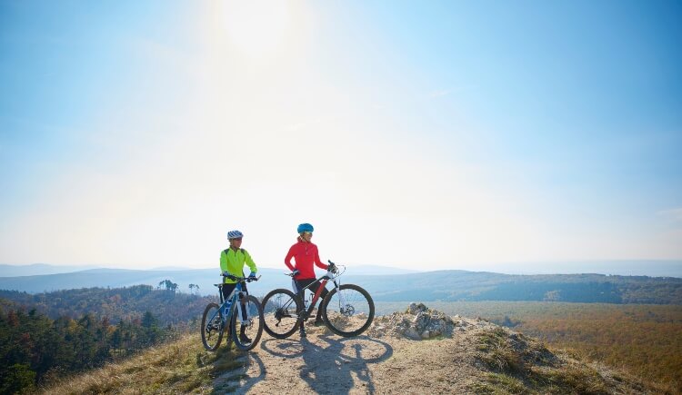 Two cyclists at the top of the hill standing with their bikes